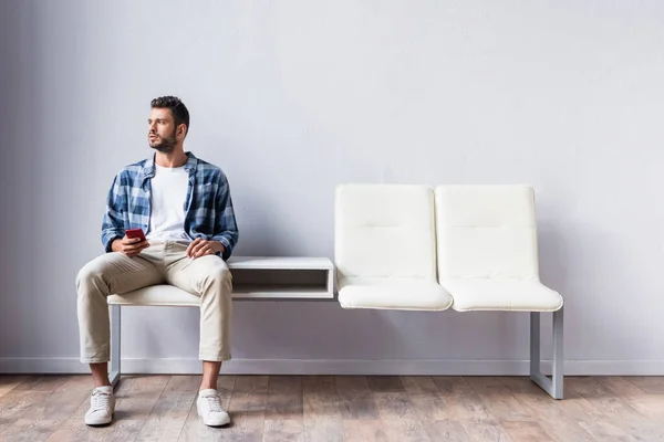 Homme tenant un téléphone portable assis sur une chaise dans le hall — Photo de stock