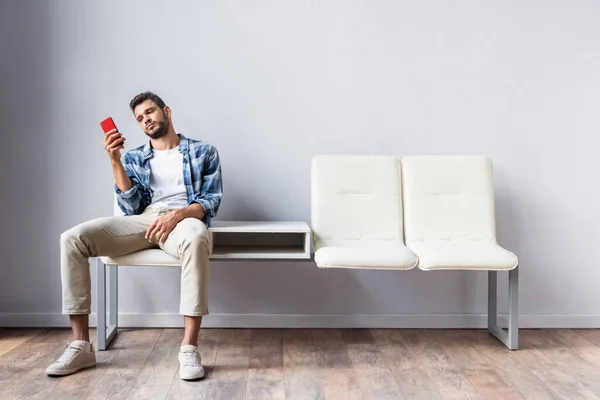 Young man using smartphone while sitting in queue near wall — Stock Photo