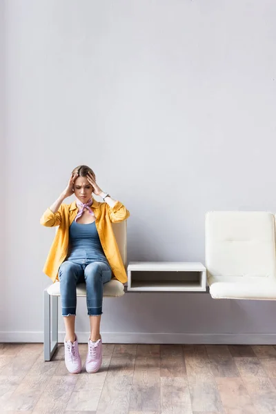 Frau leidet unter Kopfschmerzen beim Warten auf Stuhl in Halle — Stockfoto