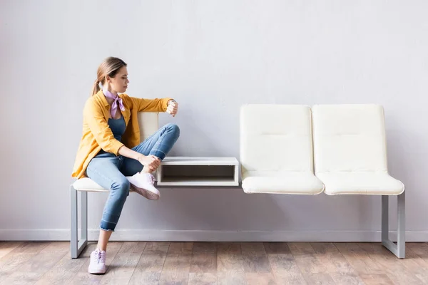 Mujer joven comprobando el tiempo en el reloj de pulsera mientras espera en la sala - foto de stock