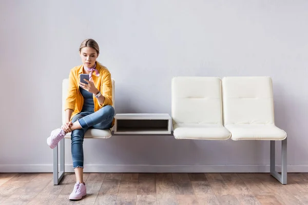 Jeune femme utilisant un téléphone portable sur la chaise dans le hall — Photo de stock