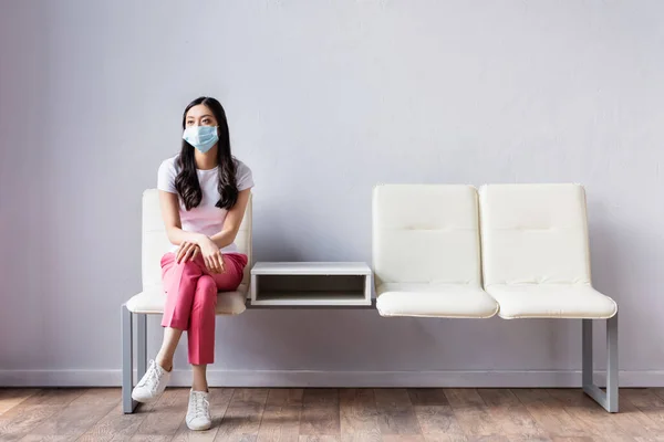 Femme asiatique dans le masque médical assis sur la chaise dans le hall — Photo de stock