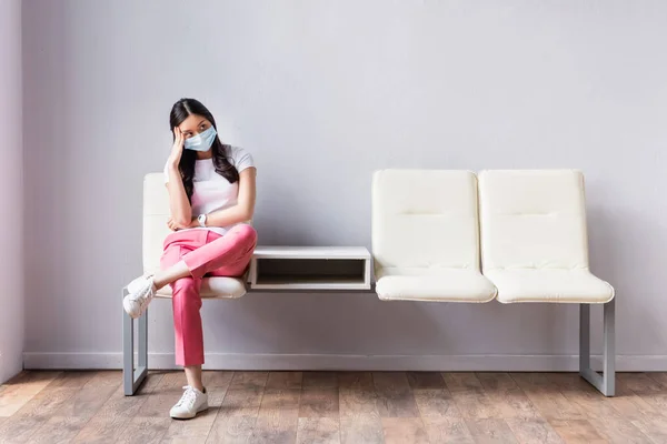 Tired asian woman in medical mask waiting on chair in hall — Stock Photo