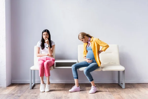Pregnant woman sitting near worried asian woman in queue — Stock Photo