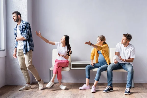 Angry multiethnic people talking to man in queue in hospital — Stock Photo