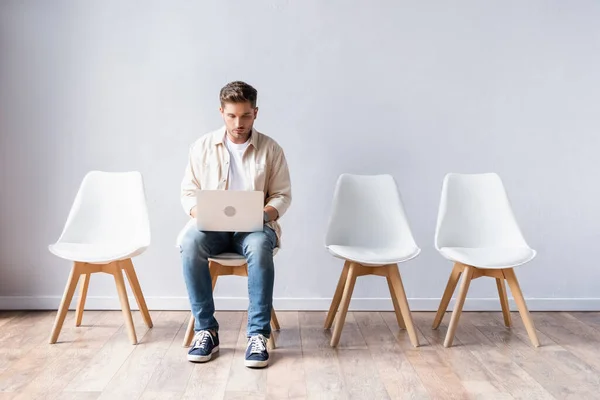 Jeune homme utilisant un ordinateur portable en attendant dans le hall — Photo de stock