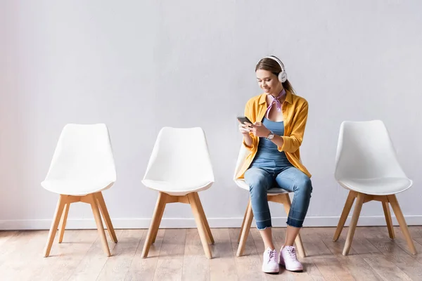 Smiling woman in headphones using smartphone in hall — Stock Photo