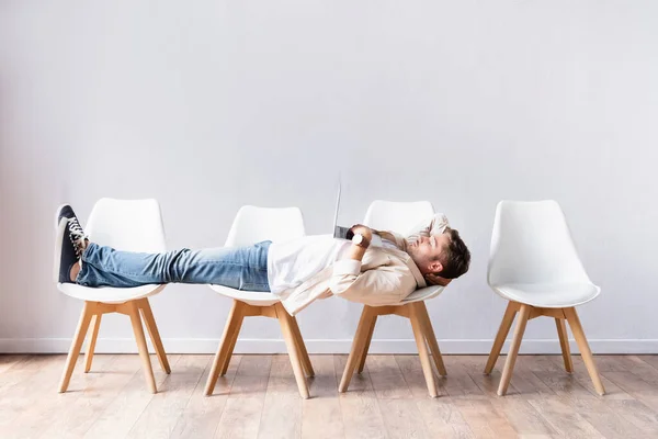 Young freelancer using laptop while lying on chairs in hall — Stock Photo