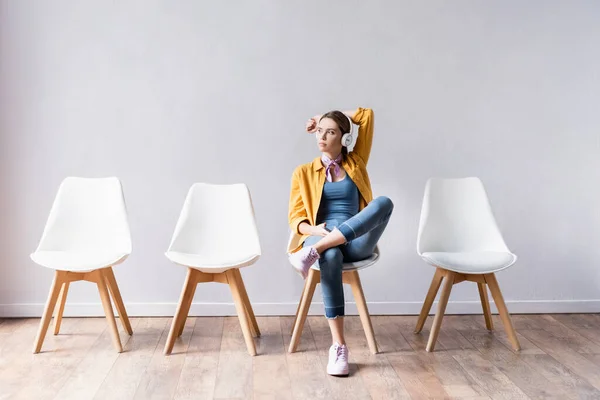 Junge Frau benutzt Kopfhörer, während sie auf Stuhl im Flur wartet — Stockfoto