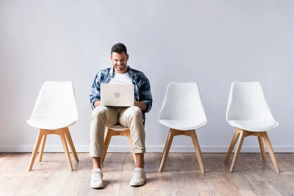 Positiver Mann arbeitet auf Laptop neben Stühlen in Halle — Stockfoto
