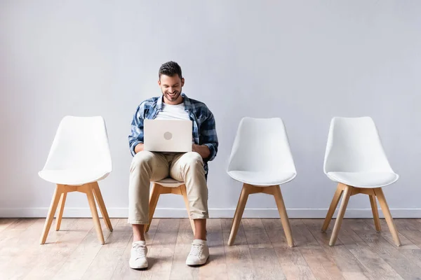 Homme positif travaillant sur ordinateur portable près des chaises dans le hall — Photo de stock