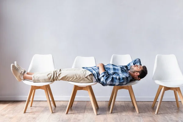 Мужчина в повседневной одежде лежит на стульях, ожидая в холле — стоковое фото