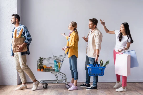 Angry multicultural customers with purchases pointing with hands in queue — Stock Photo
