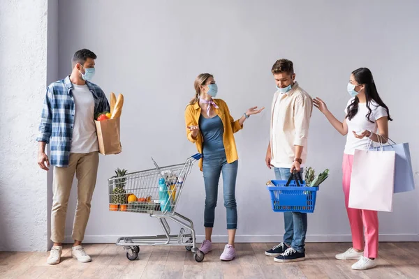 Persone multietniche in maschere mediche con cibo e borse guardando l'uomo con cesto in negozio — Foto stock