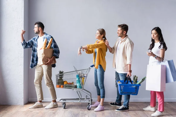 Multikulturelle Menschen mit Einkäufen gestikulieren beim Warten im Geschäft — Stockfoto