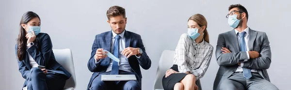Empresarios multiétnicos mirando a colega con portátil con máscara médica en la sala, pancarta - foto de stock