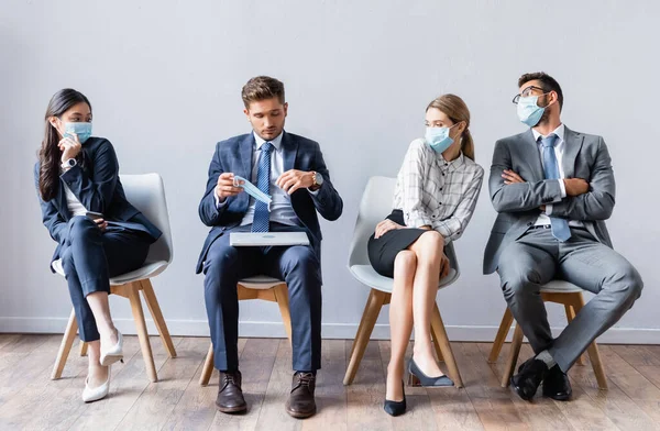 Multicultural business people in medical masks looking at man with laptop in hall — Stock Photo