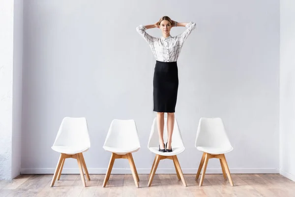 Geschäftsfrau steht auf Stuhl und blickt in Büroflur in die Kamera — Stockfoto