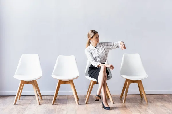 Молодая деловая женщина проверяет время, сидя со скрещенными ногами на стуле — стоковое фото