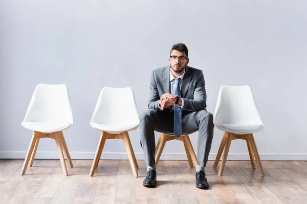 Бизнесмен с наручными часами смотрит в камеру на стуле в офисе — стоковое фото