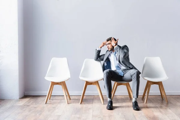 Hombre de negocios cansado apuntando a la cabeza mientras espera entrevista de trabajo en la oficina - foto de stock