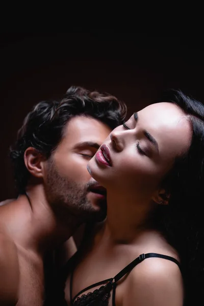 Jeune homme baisers cou de séduisante femme brune isolé sur noir — Photo de stock