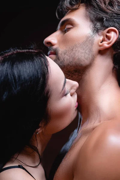Брюнетка жінка цілує шию молодого чоловіка на темному фоні — стокове фото