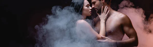 Сексуальна жінка торкається без сорочки, стоячи обличчям до обличчя на чорному тлі з димом, банер — стокове фото
