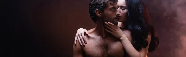 Femme sensuelle embrassant et embrassant l'homme musclé sur fond sombre avec de la fumée, bannière — Photo de stock