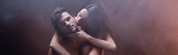 Mujer sensual abrazando cuello de hombre sexy mirando a la cámara sobre fondo oscuro con humo, pancarta - foto de stock