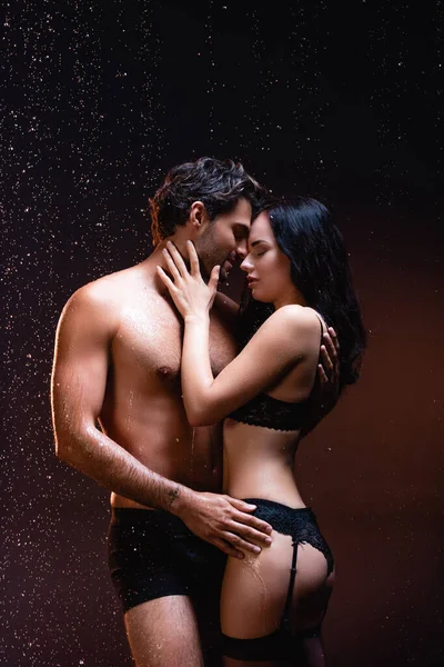 Sexy shirtless man embracing seductive woman in black lingerie and stockings on dark background — Stock Photo