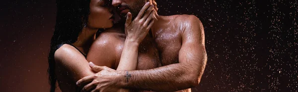 Cropped view of sensual woman hugging and kissing sexy muscular man under rain on dark background, banner — Stock Photo