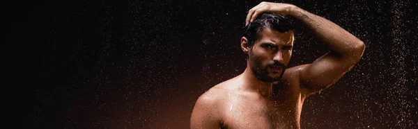 Сексуальний без сорочки чоловік під дощем дивиться на камеру на темному фоні, банер — стокове фото