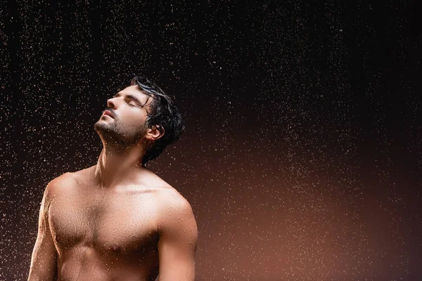 Homem sem camisa com tronco muscular em pé sobre fundo escuro sob chuva caindo — Fotografia de Stock