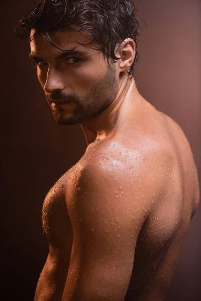 Sexy, nasser, muskulöser Mann, der auf dunklem Hintergrund in die Kamera blickt — Stockfoto