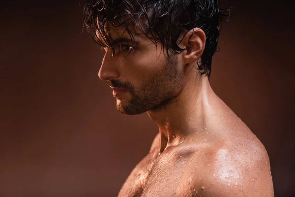 Без рубашки, мокрый мужчина смотрит в сторону, позируя на темном фоне — стоковое фото