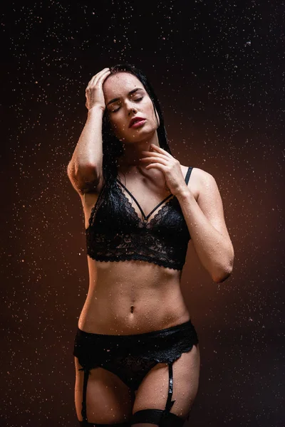 Mulher sexy em roupa interior de renda preta e meias com olhos fechados sob queda de gotas de chuva no fundo escuro — Fotografia de Stock