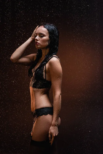 Sensual woman in black lace lingerie and stocking posing under rain on dark background — Stock Photo