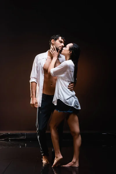 Full length view of couple in white shirts embracing while standing on wet floor on dark background — Stock Photo