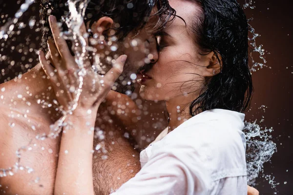 Frau küsst hemdlosen Mann in der Nähe von Wasser spritzt auf dunklem Hintergrund — Stockfoto