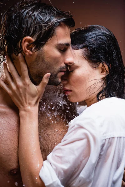 Woman in white shirt touching shirtless man near water splashes on dark background — Stock Photo