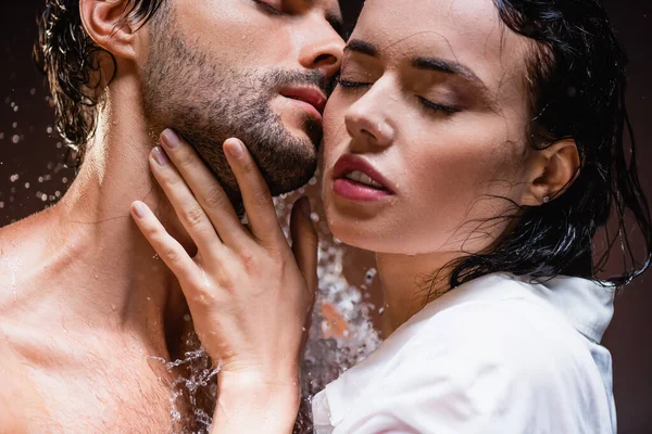 Seductive woman touching young man with closed eyes near water splashes on dark background — Stock Photo