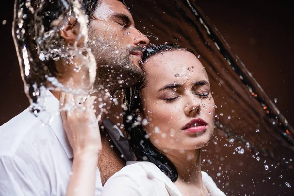 Wet man and woman standing with closed eyes near water splashes on dark background — Stock Photo