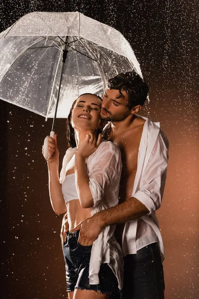 Man holding hands in pockets of happy woman standing under rain with umbrella on dark background — Stock Photo