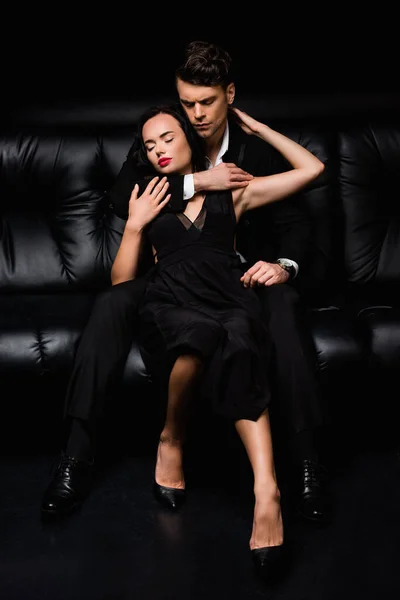 Чоловік із закритими очима обіймає молоду жінку в одязі, сидячи на чорному — стокове фото