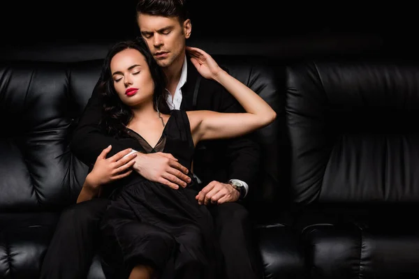 Чоловік із закритими очима обіймає молоду жінку із закритими очима, сидячи на чорному — стокове фото