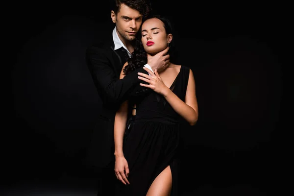Passionate man choking sexy and submissive woman in dress isolated on black — Stock Photo