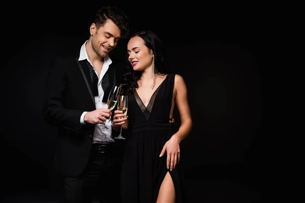 Cheerful couple holding glasses of champagne while toasting isolated on black — Stock Photo