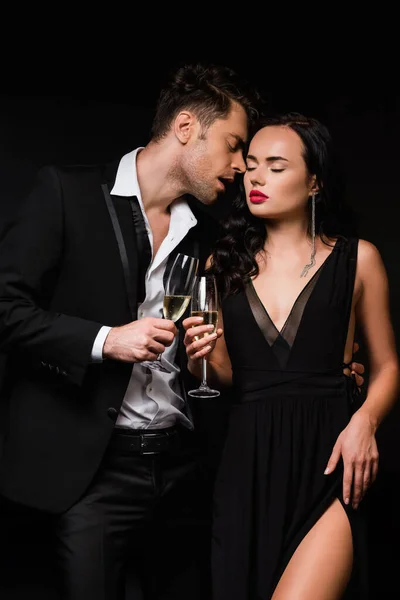 Sexy pareja sosteniendo copas de champán y tintineo aislado en negro - foto de stock