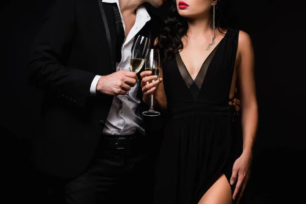 Обрізаний вид сексуальної пари, що тримає келихи шампанського, а тости ізольовані на чорному — стокове фото
